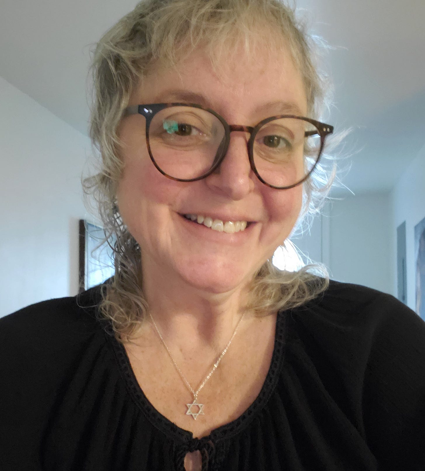 A white woman with gray hair and round glasses sporting a Jewish star necklace. 