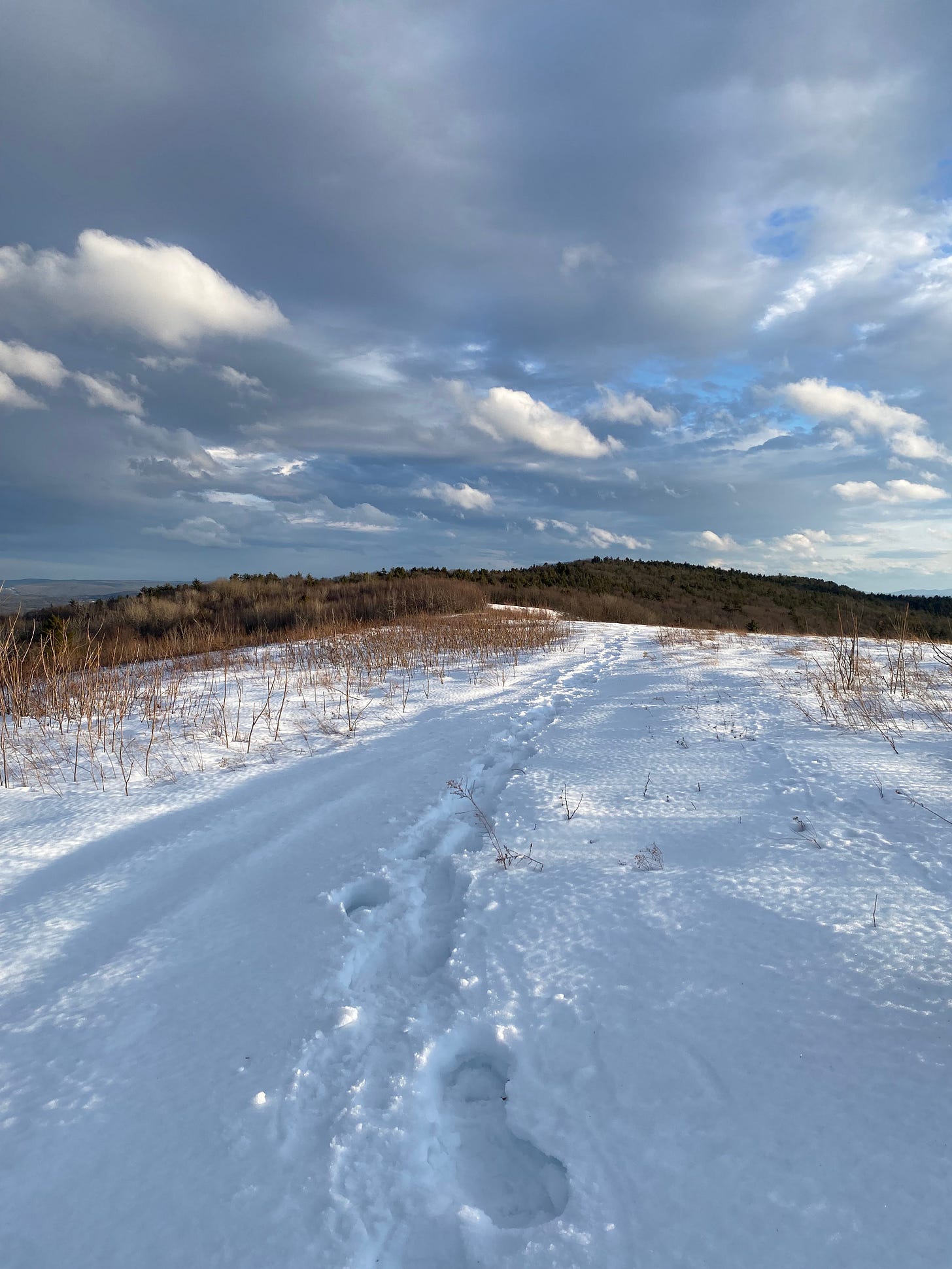 A snow-covered field on the top of a ridge under a cloudy sky.