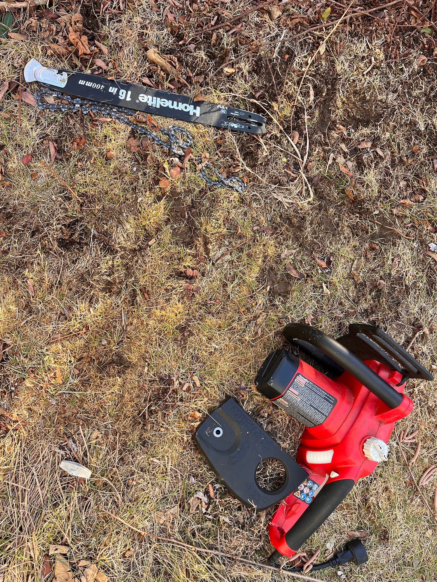 Pieces of a disassembled chainsaw with a red body on the brown lawn