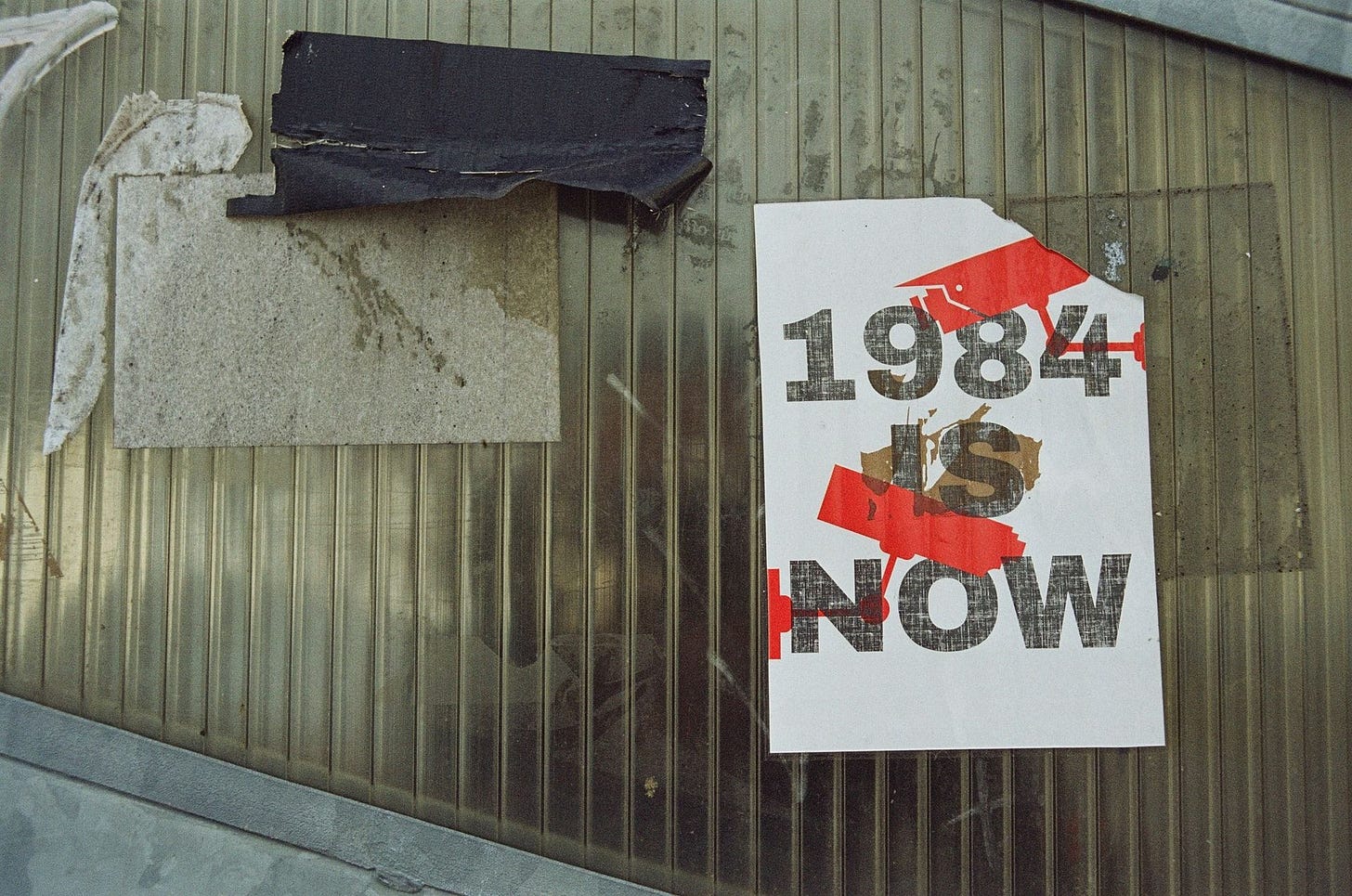 Muro com restos de cartazes em que um deles diz: 1984 is now (Tradução: 1984 é agora). Muro com restos de cartazes em que um deles diz: 1984 is now (Tradução: 1984 é agora).