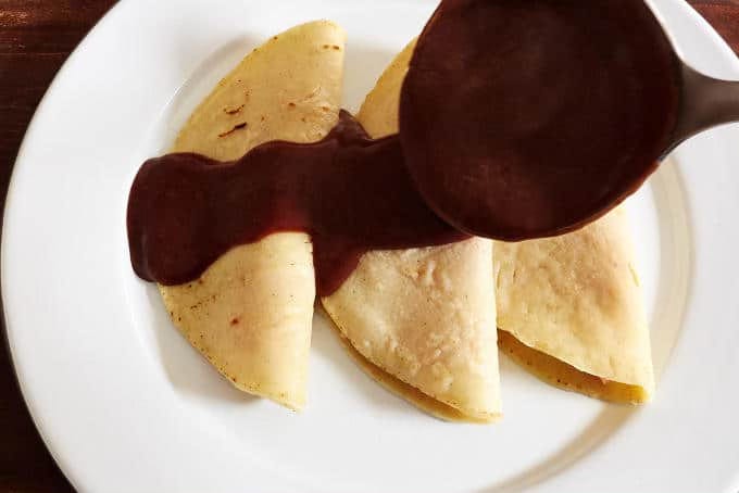 Spooning bean enchilada sauce on tortillas