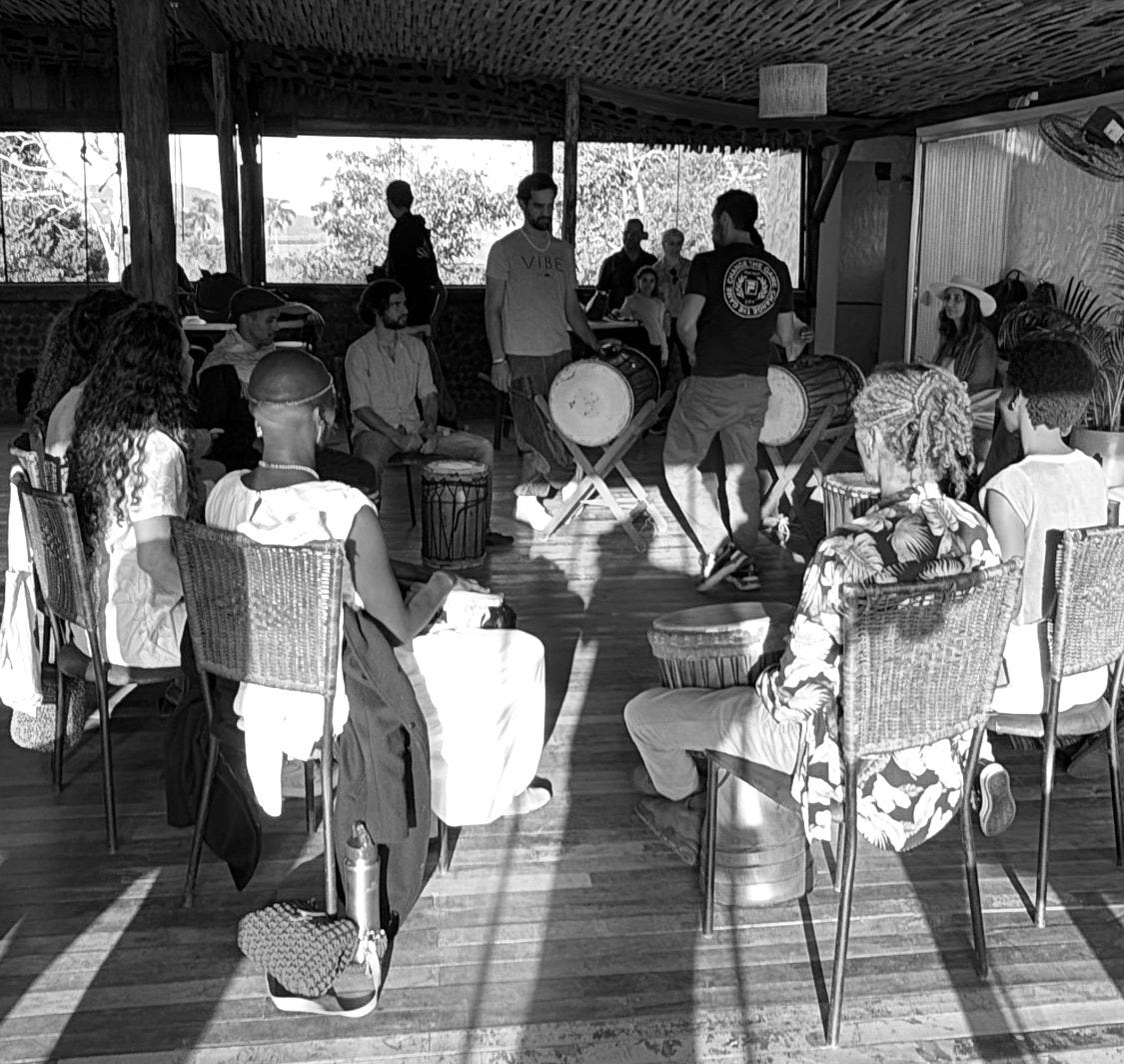 People with drums in a circle under a woven bamboo pavilion