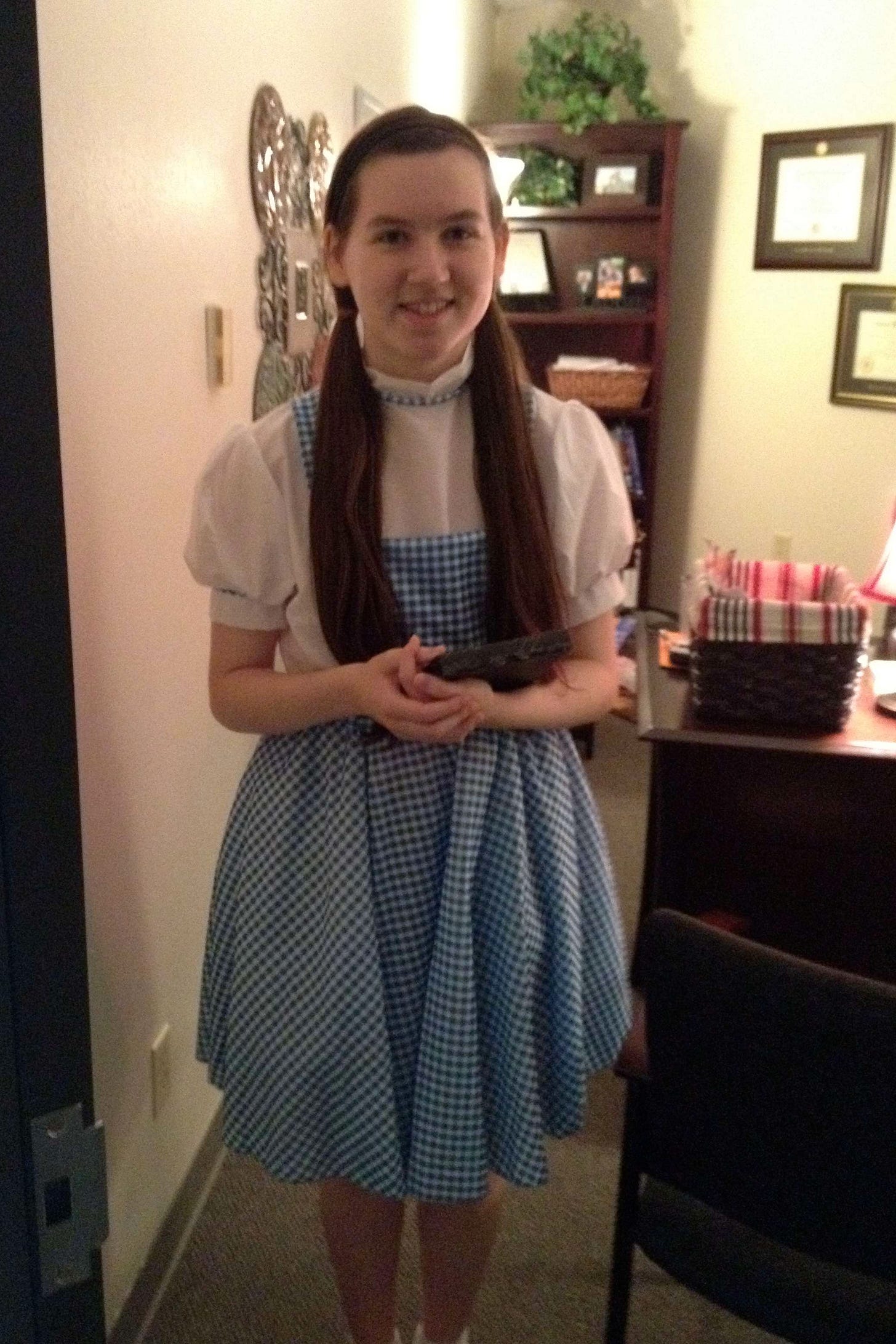 13-year-old Harper in a Dorothy costume. Her long brown hair is in pigtails and she is holding a plaque in her arms. 