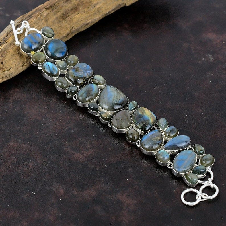 May include: A silver bracelet with a row of dark blue and green labradorite gemstones. The bracelet has a lobster claw clasp.