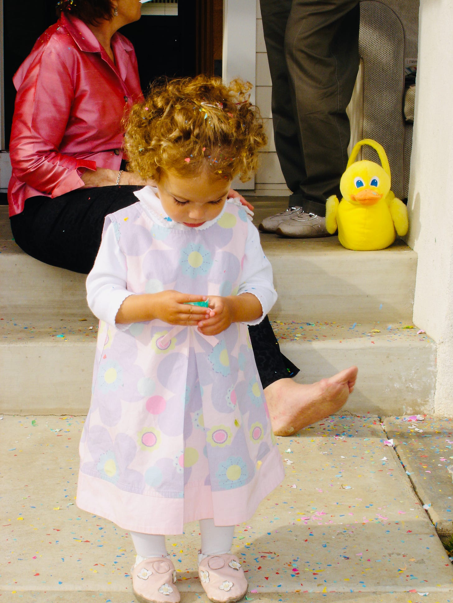 A little girl in an Easter dress standing in confetti on the front steps with a ruber duck basket. A little girl in an Easter dress standing in confetti on the front steps with a ruber duck basket.