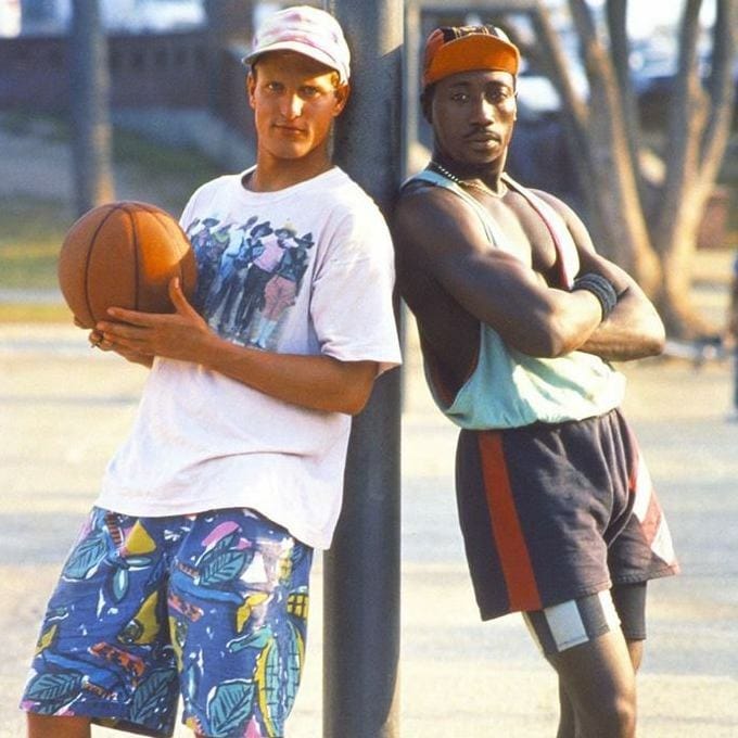 Woody Harrelson holds basketball while leaning against a basketball pole opposite Wesley Snipes in the 1992 film "White Men Can't Jump"