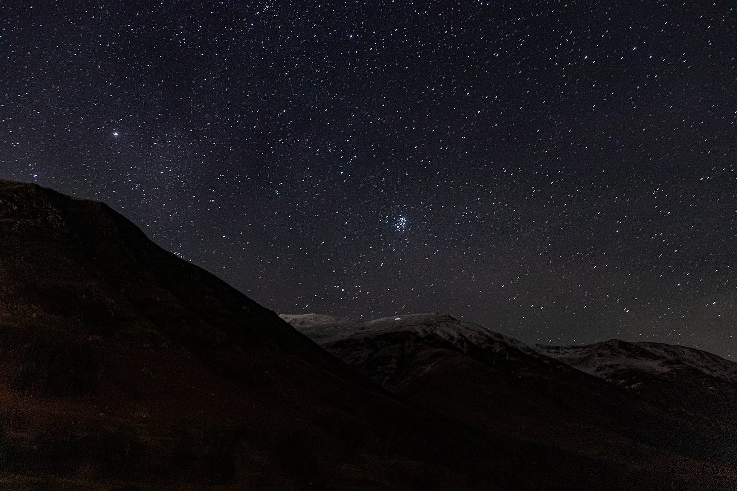 A photo of a star-filled night sky with the silouette of a mountain in the foreground. The mountain is snowcapped, and a smear of light is visible from a headtorch. A photo of a star-filled night sky with the silouette of a mountain in the foreground. The mountain is snowcapped, and a smear of light is visible from a headtorch.