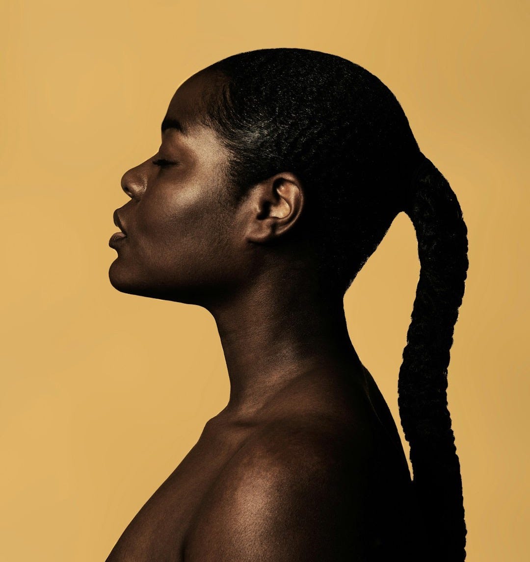 braided woman taking photo beside yellow painted wall