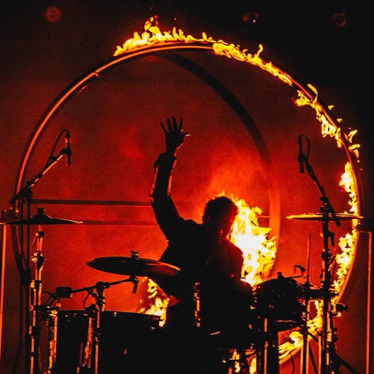 This may contain: a man with his arms in the air behind a drum set on fire and flames This may contain: a man with his arms in the air behind a drum set on fire and flames