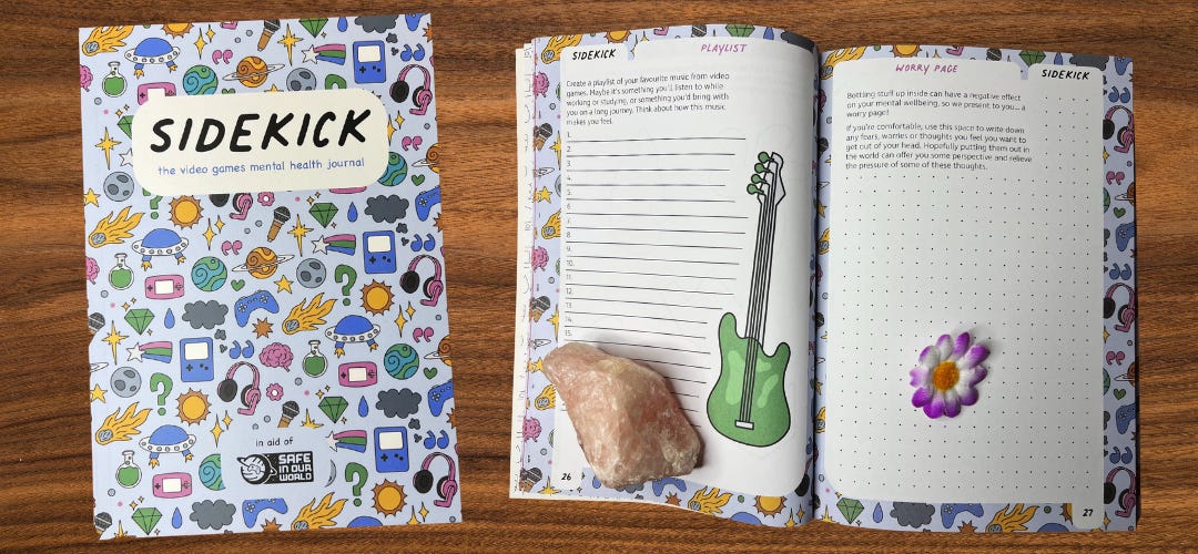 Sidekick: The Video Games Mental Health Journal. A copy lays open to two journaling prompts about mental health and gaming and another copy lays closed on a wooden surface.