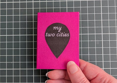 image 1; a small booklet held in a woman's hand, the cover is magenta pink with a black map pin in the center and the words "my two cities" in white. image 2, a woman's hand holds up the booklet, the spread shows to similar photos. the photo on left shows a large flowering tree with bright pink and white blooms behind the tree is a house with faded yellow wood siding, on the right the photo shows a small flowering tree with bright pink and white blooms, behind the tree is an apartment building made of pale yellow stucco. image 3, a woman's hand holds open the booklet, the spread shows two similar photos. the photo on the left shows a gothic archway through the archway we see stairs leading up to trees and a lone figure silhouetted, the photo on the right shows a tall carved stone archway, there are people in the foreground and through the archway we see a pale sky a long statue silhouetted. image 4, a woman's hand holds up the booklet, the spread shows two similar photos, the photo on the left shows various posters and flyers interspersed with graffiti on a dark brown door, the photo on the right shows a wall completely covered in flour pasted flyers and posters. image 5, a woman's hand holds up the booklet, the spread shows two similar photos, the photo on the left shows an iced coffee drink in a plastic cup and a iced blueberry scone on.a black napkin on a rustic wood table with an empty wood cane chair in the background, the photo on the right shows an iced coffee drink in a glass mason chair and a croissant covered in powdered sugar on a black stone tray sitting on a smooth wooden table, there's am empty white woven chair in the background. image 6, a woman's hand holds up the booklet, the spread shows two similar photos, the image on the left shows the tops of trees and small homes and flat top apartment buildings, the sky is pale yellow and blue and a few dark blue clouds dot it, the image on the right shows the tops of white homes and apartments with dark red terracotta shingles on the roofs, the sky is pale blue and yellow with dark blue and bright pink clouds. image 7, a woman's hand holds open the booklet, the spread shows two similar photos, the photo on the left shows a white gallery wall featuring many framed art works in varying sizes and shapes. a long man in a khaki shorts and blue shirt stands to the left looking up at the artwork, the photo on the right shows a large beige curved wall featuring many hanging loose canvases painted in bright warm colors, a lone man stands to the right in all black looking up at the canvases. image 8, a woman's hand holds open the booklet, the spread shows two similar photos, the photo on the left is a woman's left hand holding an ice cream cone with two scoops, the ice cream is white with brown flecks, the background shows a blurry concrete sidewalk, the photo on the right show's a woman's left hand holding an ice cream cone, the ice cream is dark chocolate and artfully arranged into petals to resemble a rose, the background is a blurry tiled sidewalk in white and black. image 9, a woman's hand holds open the booklet, the spread is two similar photos, the photo on the left is a bright blue sky with fluffy white clouds over the NYC skyline, the photo on the right shows the sky in the exact same bright blue shade with white fluffy clouds that seem to connect with the clouds from the photo on the left, the buildings at the bottom of the photo are white with bright red terracotta roofs