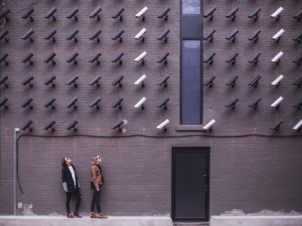 two women facing security camera above mounted on structure