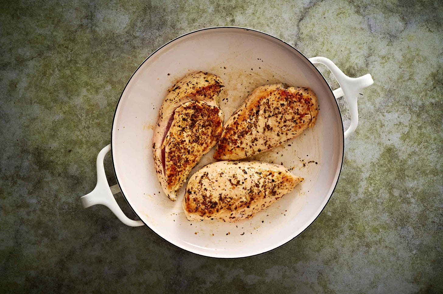 Step 1 of making Lemon chicken orzo pasta showing chicken seasoned and searing in a white pan on a marble counter.