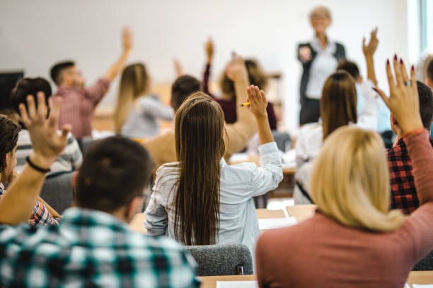 Back view of college students raising their arms on a class at lecture hall.