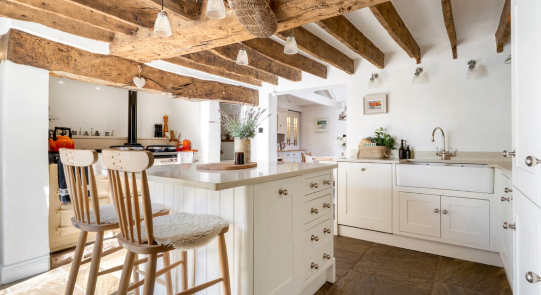 A kitchen with wooden beams, a kitchen island, white cabinets, and white walls