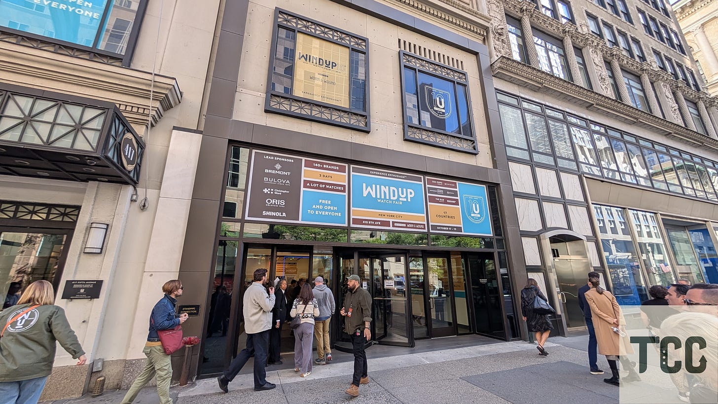 Photograph of the exterior of Center415 in Midtown Manhattan, showing the entrance to Windup Watch Fair 2025. Event signage highlights sponsors and statistics (“140+ brands,” “17 countries”), and a line of attendees waits to enter.