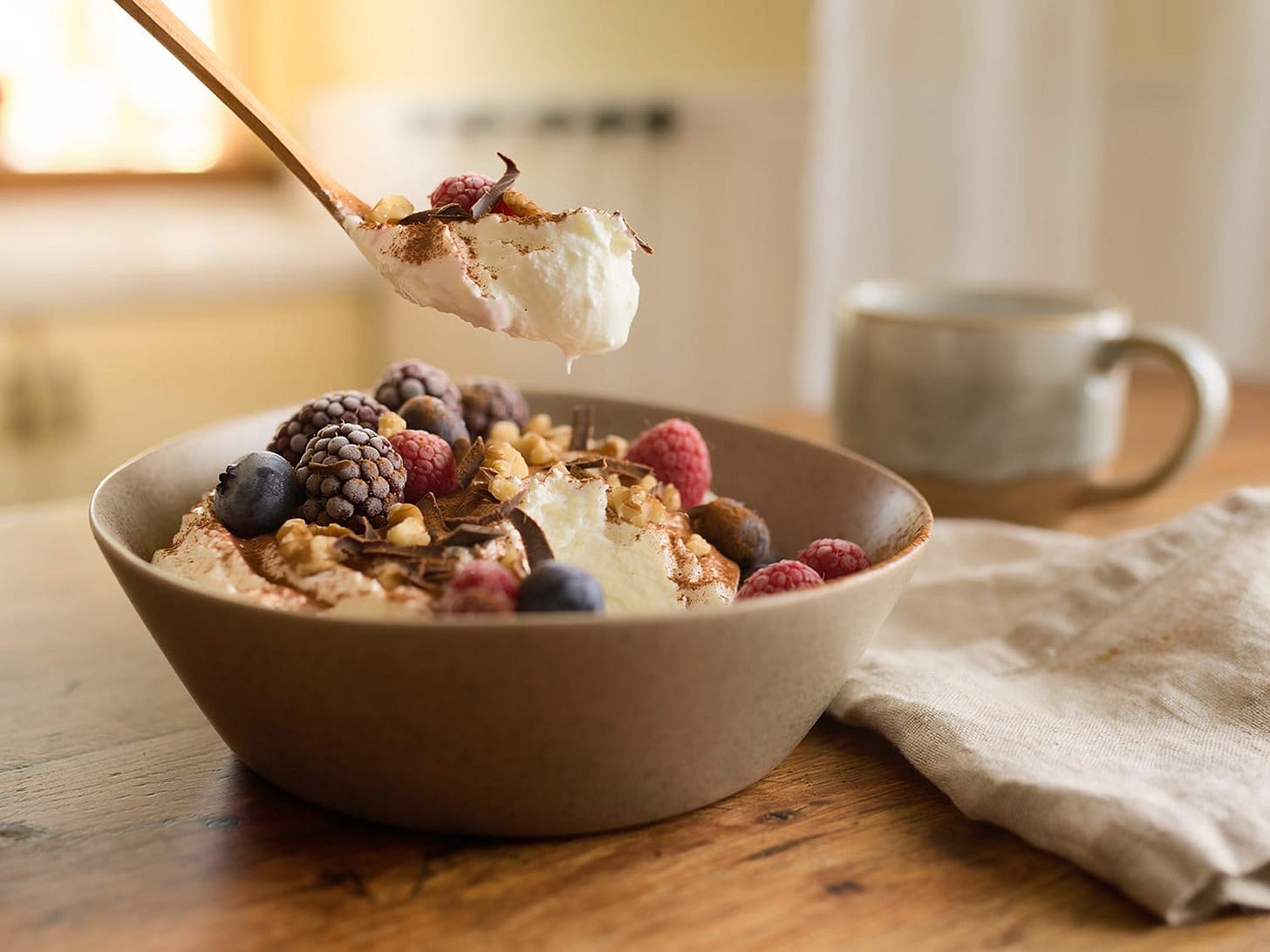 A photograph of a bowl of Greek yogurt topped with berries, walnuts and chocolate flakes. A photograph of a bowl of Greek yogurt topped with berries, walnuts and chocolate flakes.
