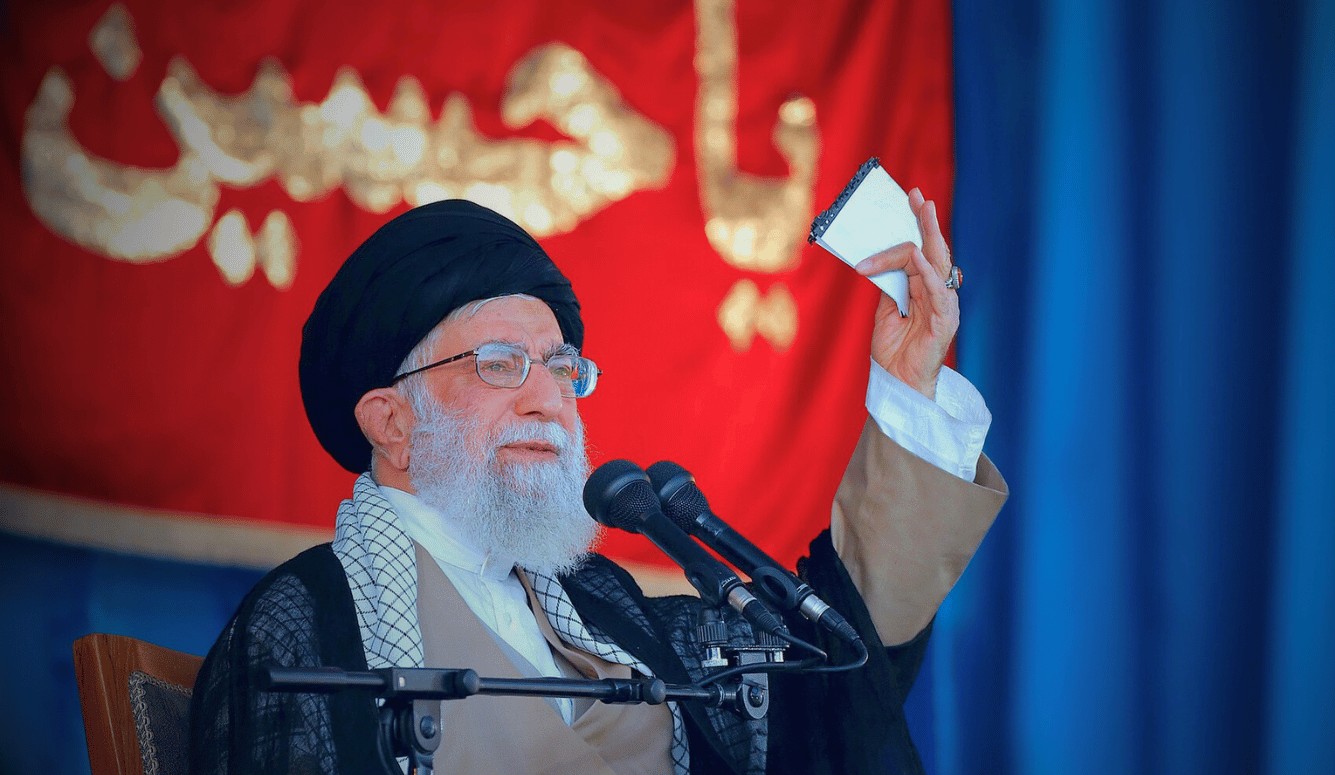 Ayatollah Ali Khamenei speaking at Basij conference, holding note beside microphones, red backdrop, Azadi Stadium 2018 Ayatollah Ali Khamenei speaking at Basij conference, holding note beside microphones, red backdrop, Azadi Stadium 2018