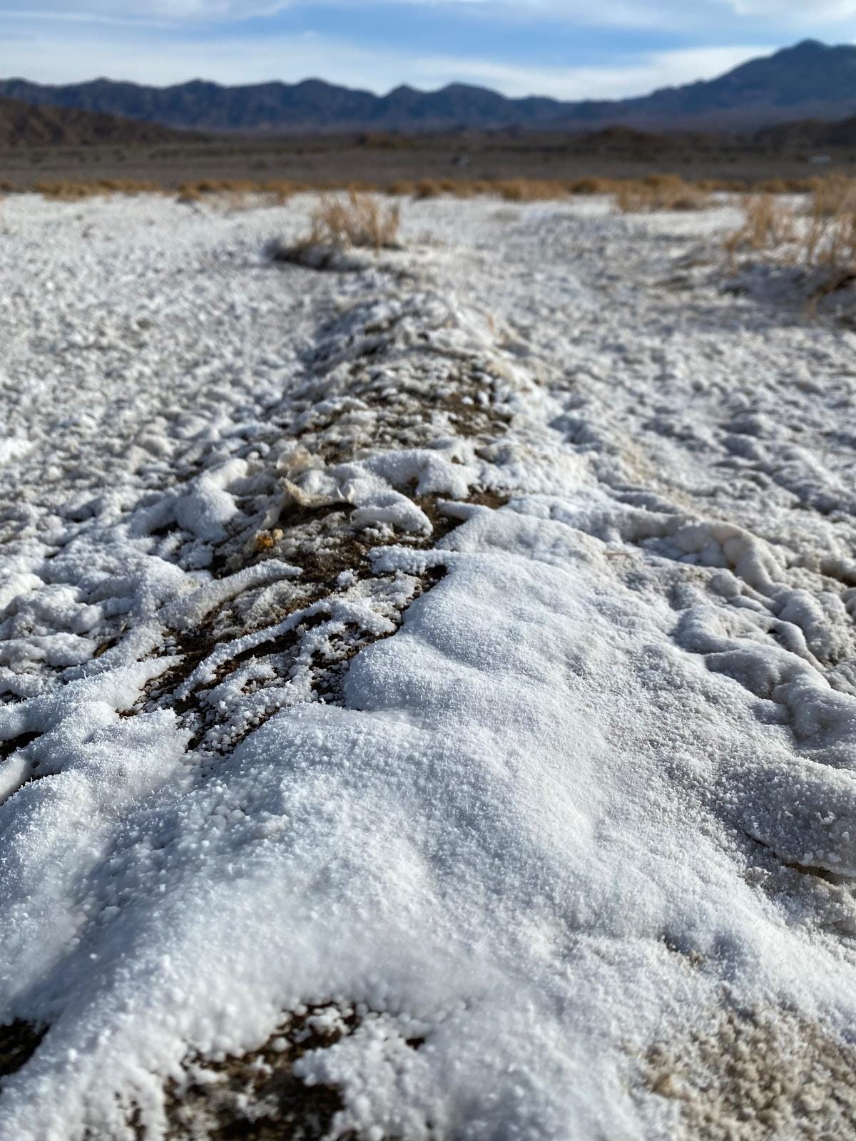 Depósitos brancos de sal seco e rachado no chão da Badwater Basin, Vale da Morte, Califórnia, com montanhas secas ao fundo. Ilustra a extrema evaporação e a origem dos minerais.