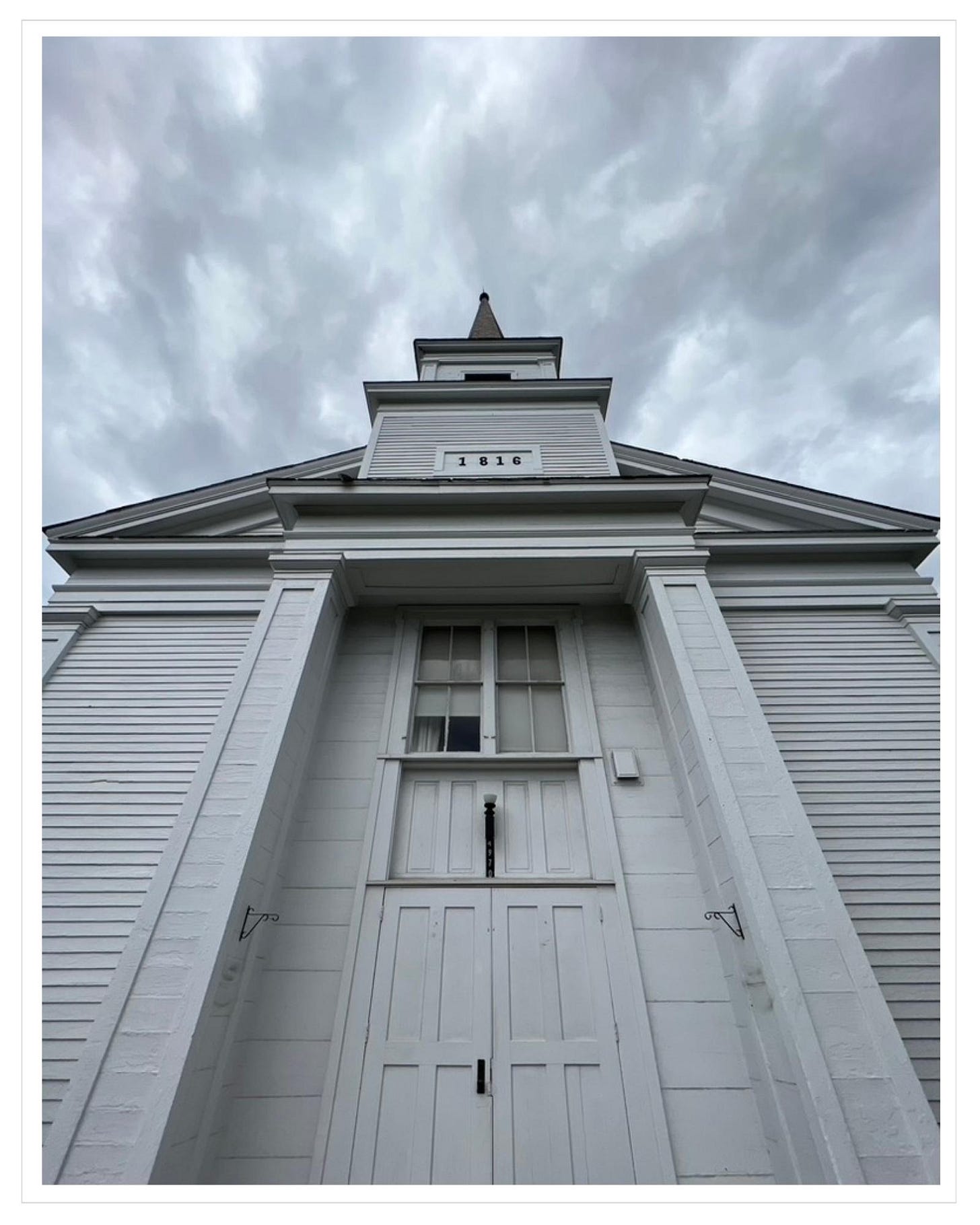 Historic church entrance and steeple, striations of dark grey clouds