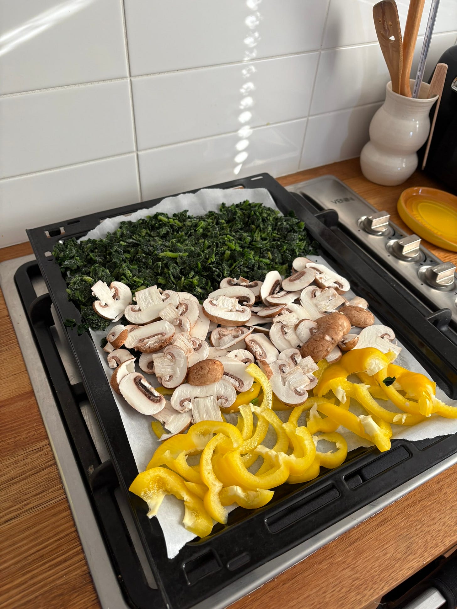 A tray of vegetables ready for the oven including sliced brown mushrooms, a yellow capsicum and frozen spinach.
