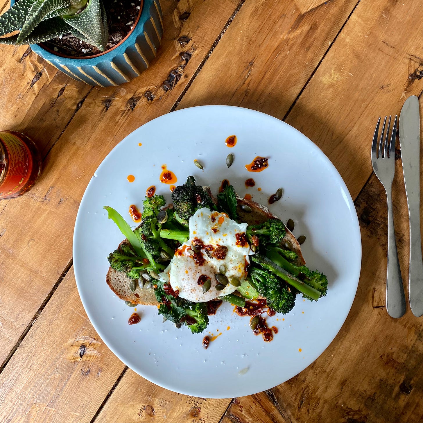 White plate serving sourdough toast topped with broccoli, poached egg, chilli oil and toasted pumpkin seeds
