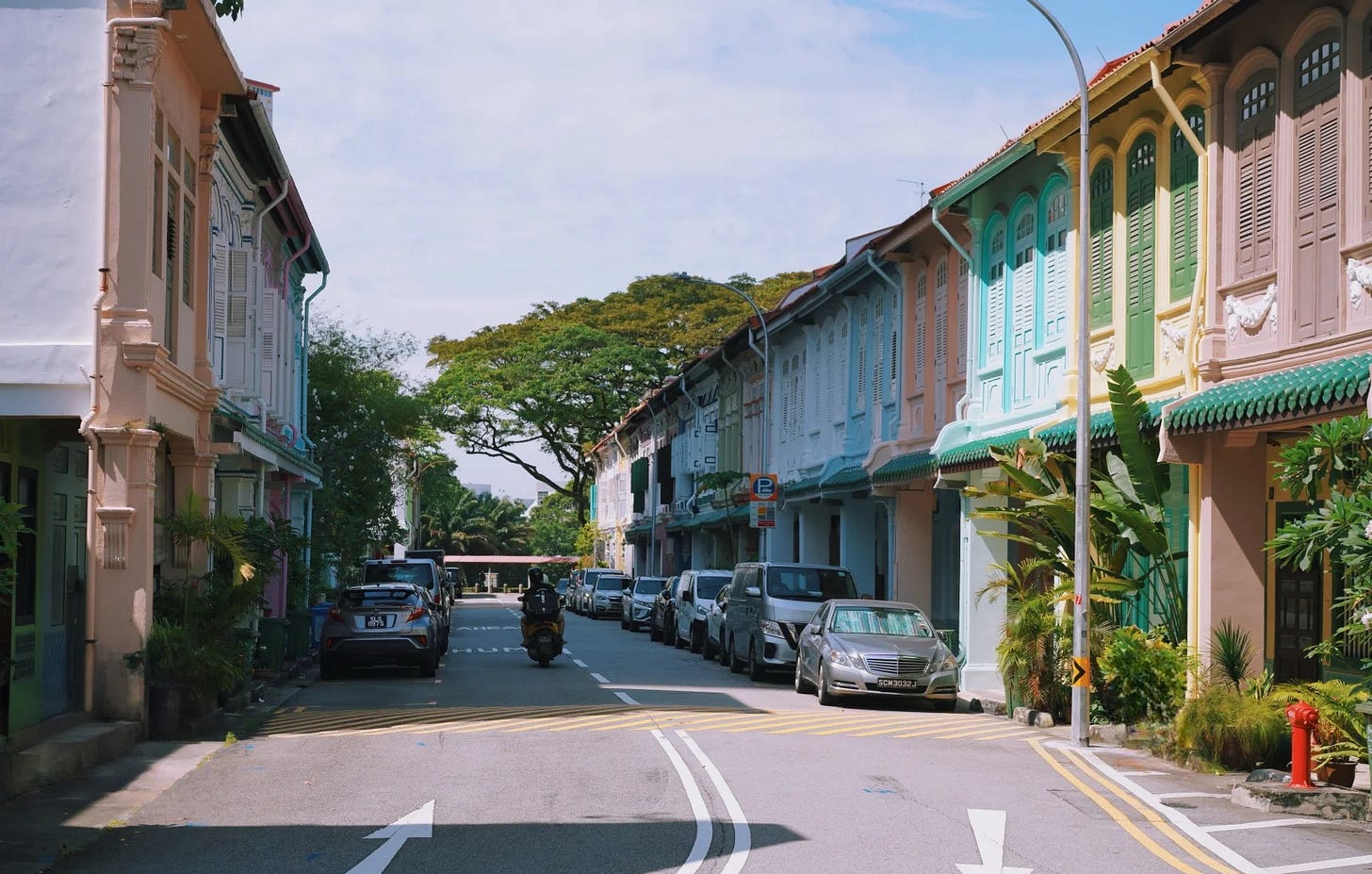 A quiet street of pastel Peranakan shophouses in Singapore, with shuttered upper windows and parked cars along the kerb. A quiet street of pastel Peranakan shophouses in Singapore, with shuttered upper windows and parked cars along the kerb.
