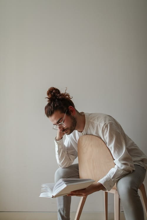 Free A Man Sitting on a Chair while Reading a Book Stock Photo
