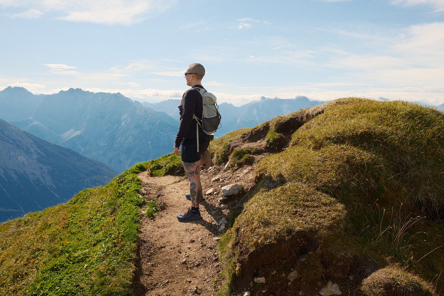 Image of woman with shaved head standing on a path with mountains in the background