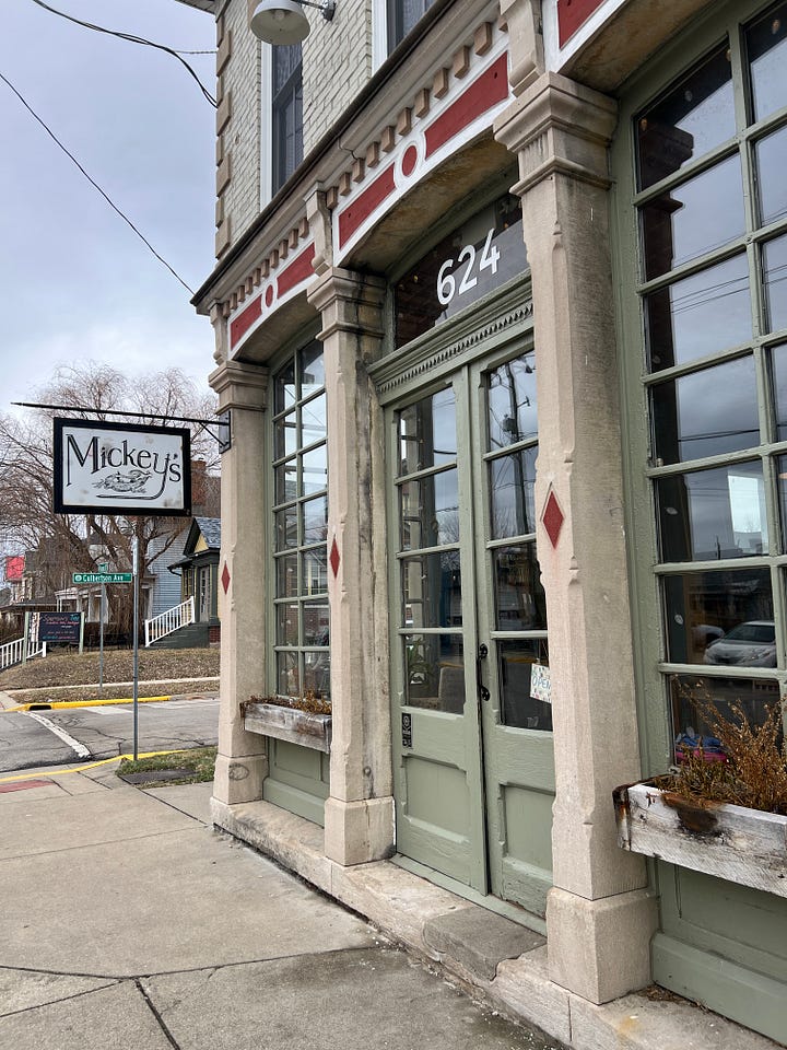 Left: The outside of Mickey's, showing an old stone building with tall green doors and lots of windows. Right: The inside of Mickey's, showing lots of mismatched tables and chairs and bookshelves everywhere. 