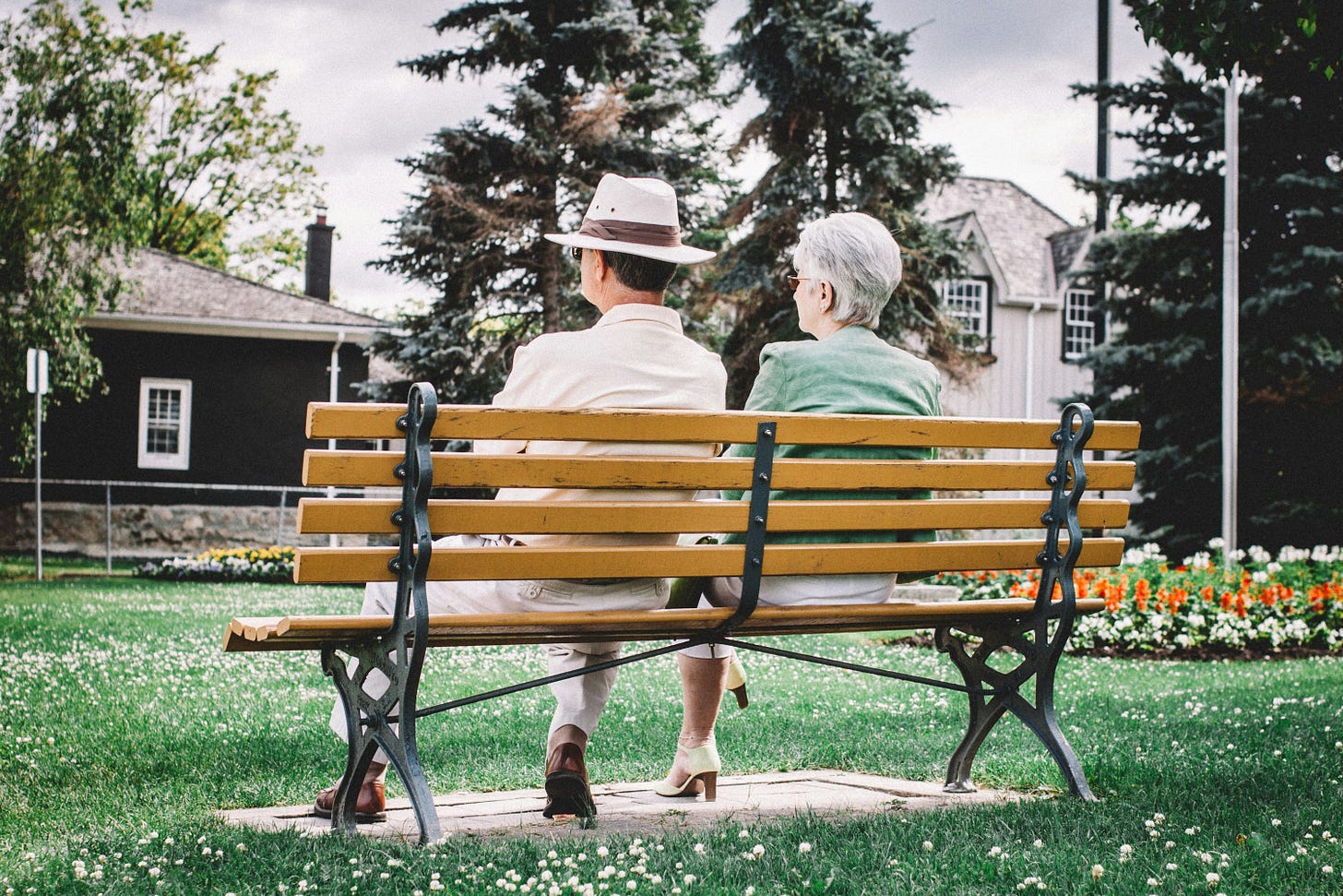 Retired couple sitting on park bench contemplating pension regret and retirement anxiety in peaceful suburban setting Retired couple sitting on park bench contemplating pension regret and retirement anxiety in peaceful suburban setting
