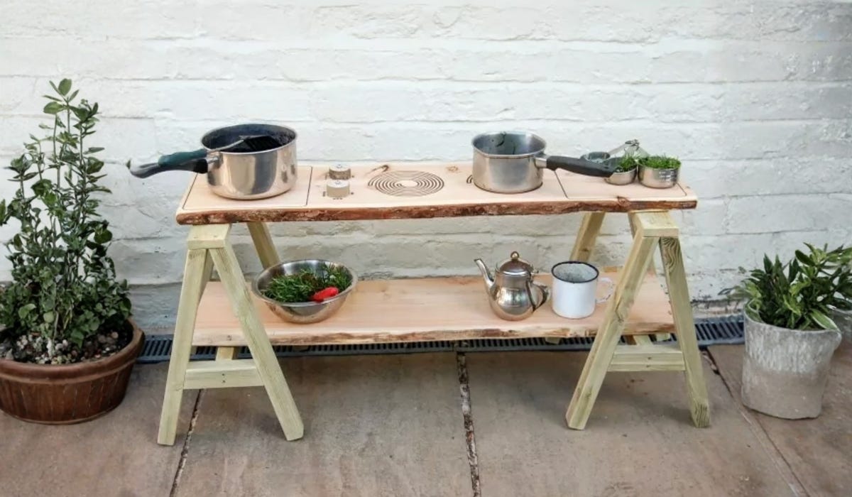A mud kitchen set up, with pots and pans, against a painted white brick wall