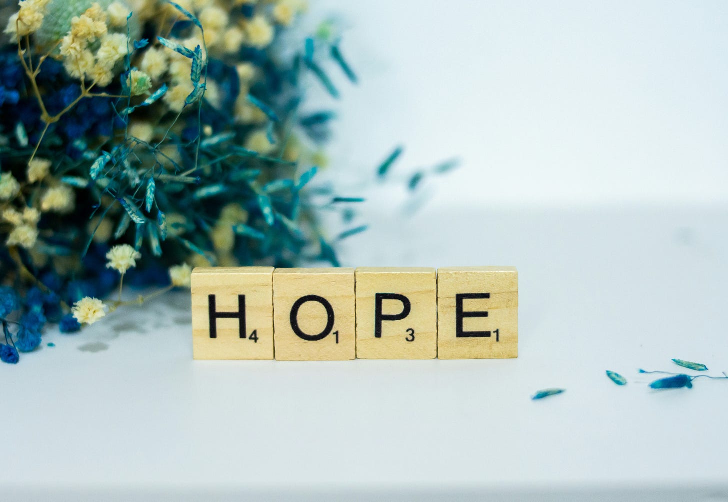 Image of four wooden game tiles spelling out HOPE with some flowers gathered behind.