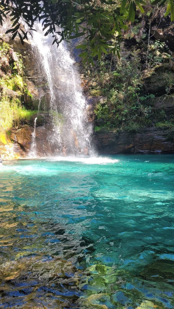 Foto de uma cachoeira não tão alta, mas cuja água cai num poço de águas belíssimas azul-turquesa.