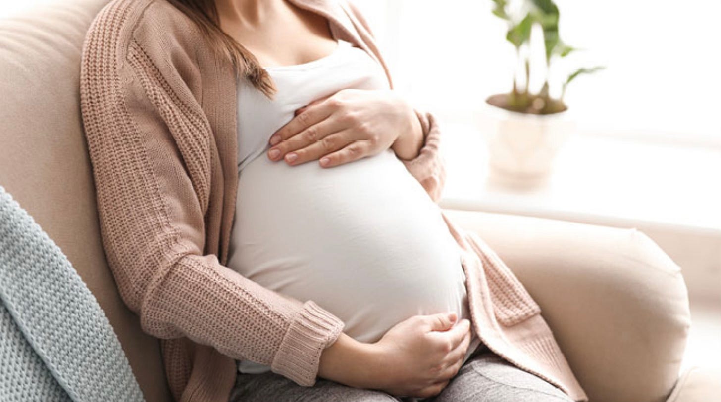Seated pregnant woman caressing her baby bump.