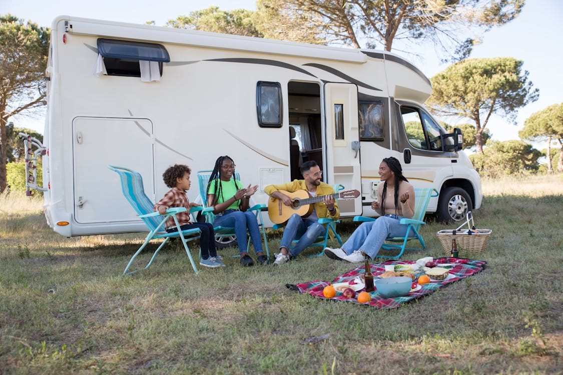 Free A family relaxing outdoors with a picnic and guitar by their camper, enjoying a sunny summer day in Portugal. Stock Photo