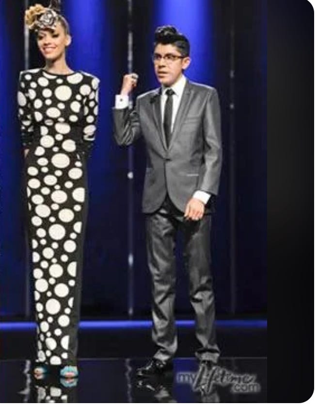 Mondo in glasses and a suit stands next to his model with the polka dot dress, sleeves intact. Mondo in glasses and a suit stands next to his model with the polka dot dress, sleeves intact.