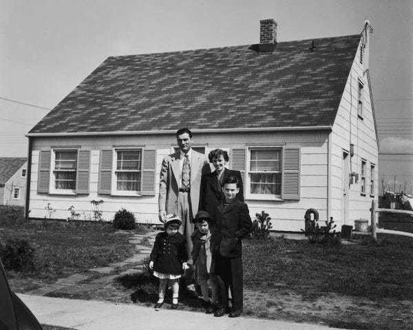 This may contain: a black and white photo of three people standing in front of a house with two children