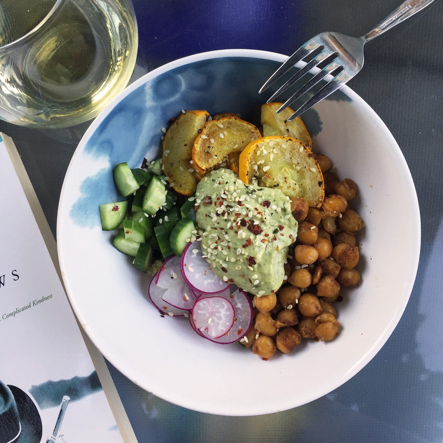From above, a bowl of the salad described above with each element in a little pile on top of the quinoa & kale. Hemp hearts, sesame seeds, and aleppo pepper flakes sprinkled on top. To the left of the bowl is a stemless glass of white wine and the corner of a paperback novel.