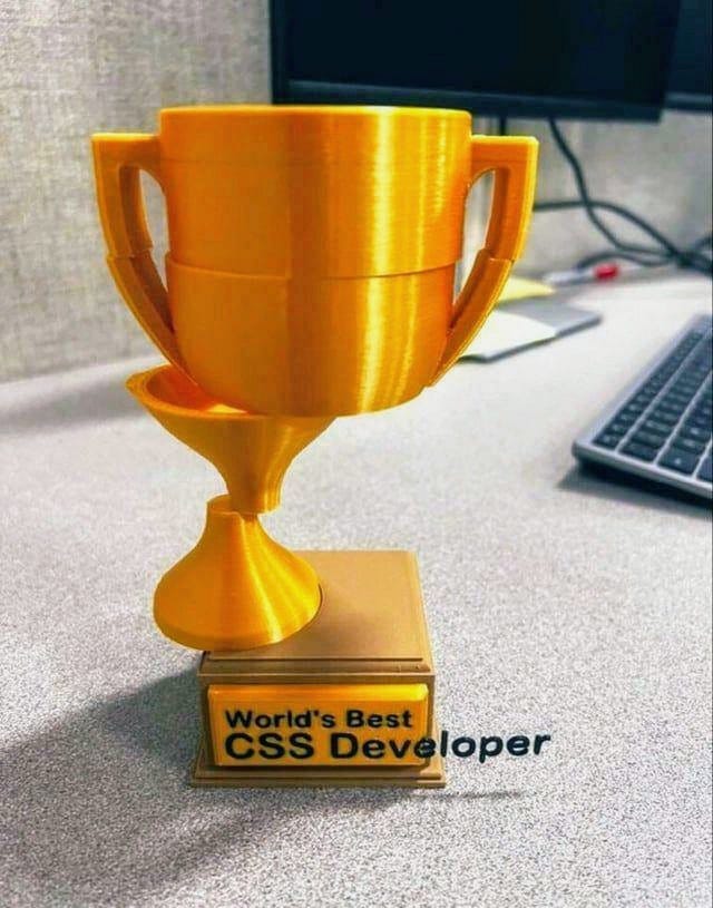 Meme: Pohár pro nejlepšího CSS vývojáře na světě. Pohár je ale rozřezaný vodorovně na čtyři části, které jsou vůči sobě posunutí. Stojí jen polovinou na podstavci, na kterém ne nápis uvedený tak, že slovo vývojář přetéká mimo hmotu podstavce. Obrázek si dělá legraci ze špatného zarovnávání layoutů v CSS.