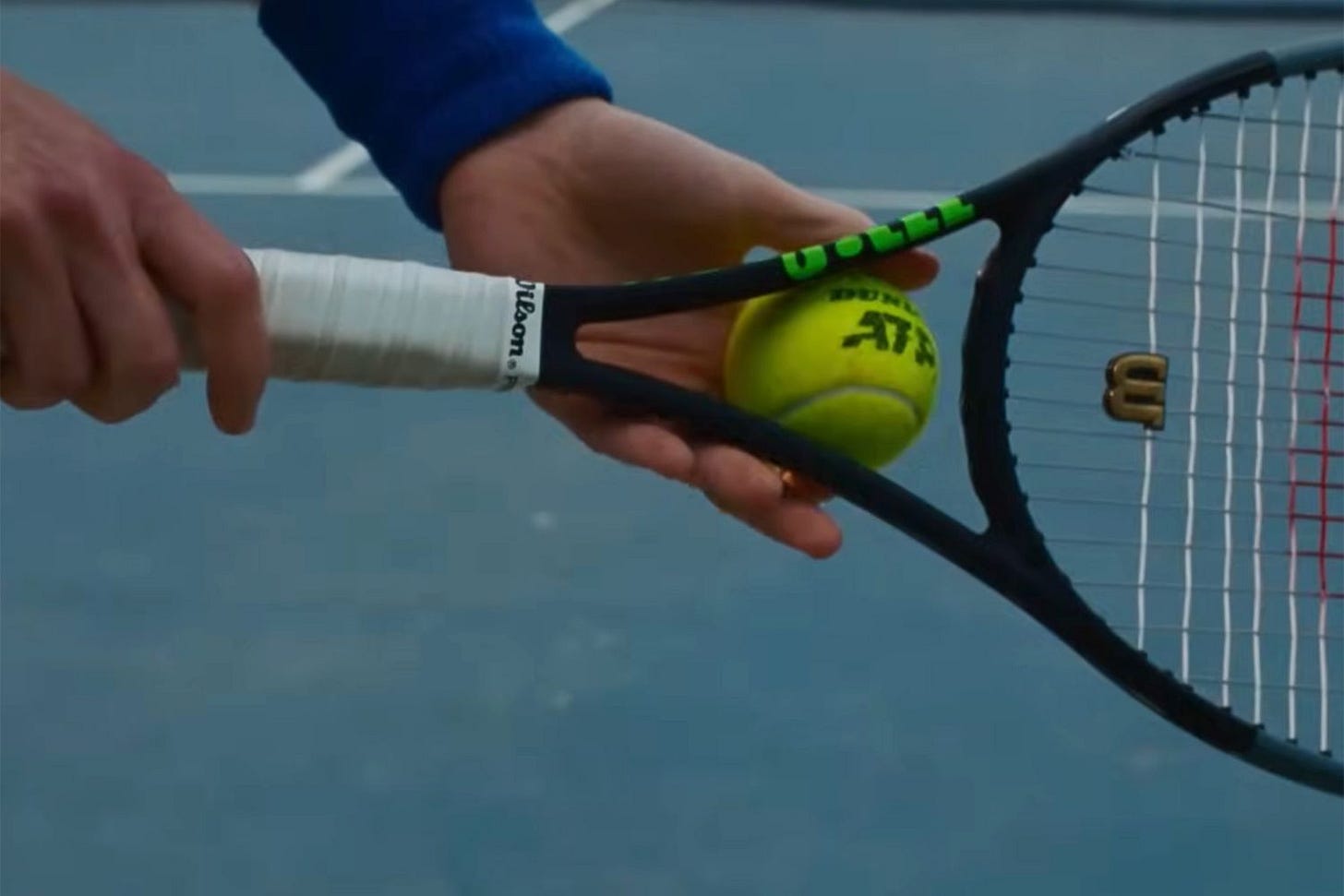 A man holds a tennis ball at the center of a tennis racket.