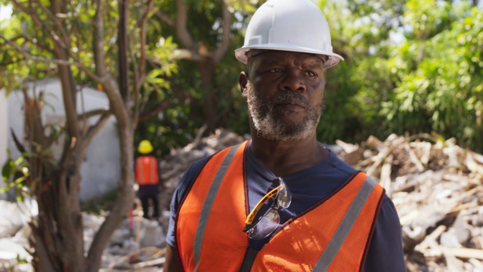 Man in a hardhat and yellow vest. Behind him is the wreckage from a recent demolition