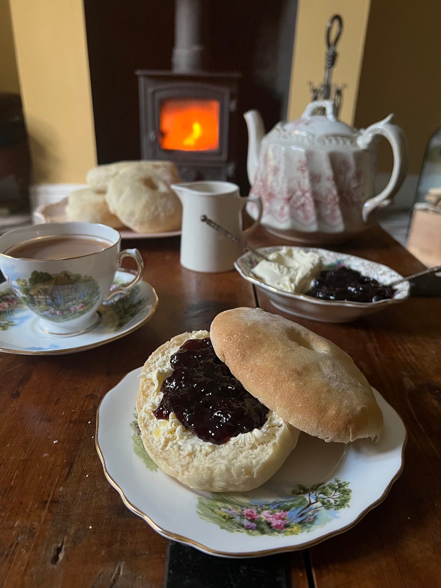 split Huffkin (bread roll) with cherry jam and clotted cream on a tea table with fire in background