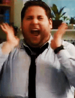 A Gif of jonah hill wearing a white shirt looking from left to right in excitement with his hands raised