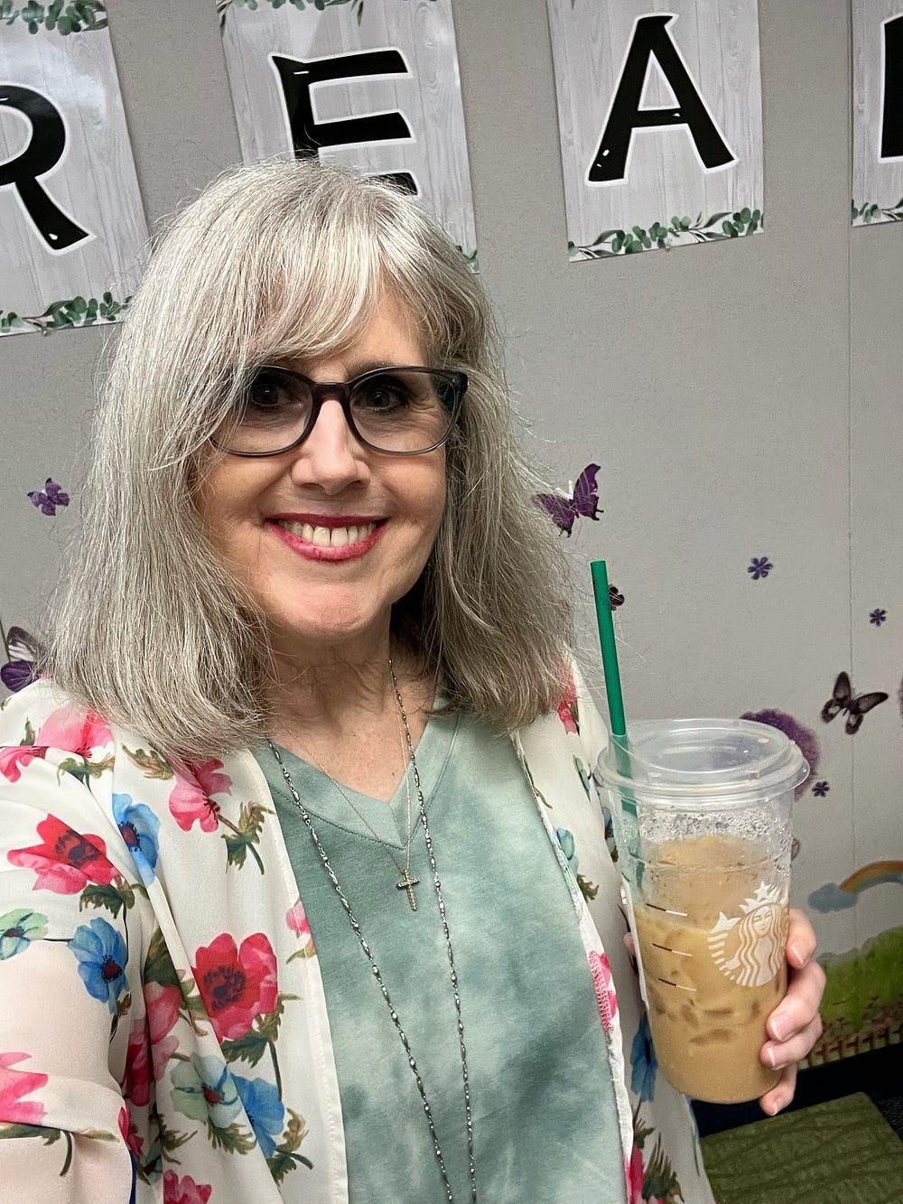 The author is standing in her classroom,holding an iced coffee and smiling.