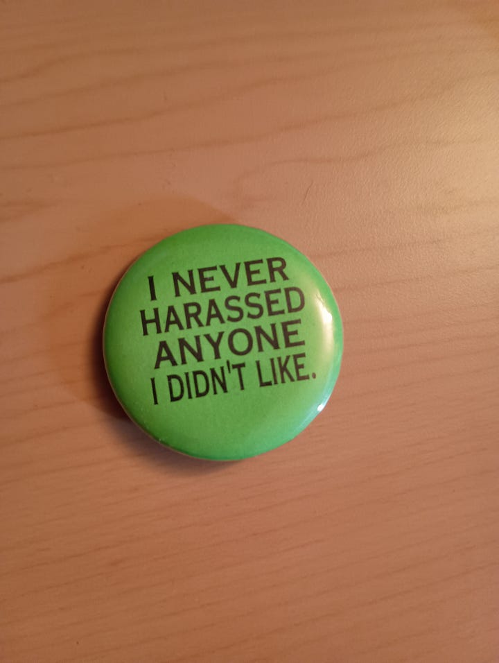 A baby side-eyeing a green pin that says I never harrassed anyone I didn't like