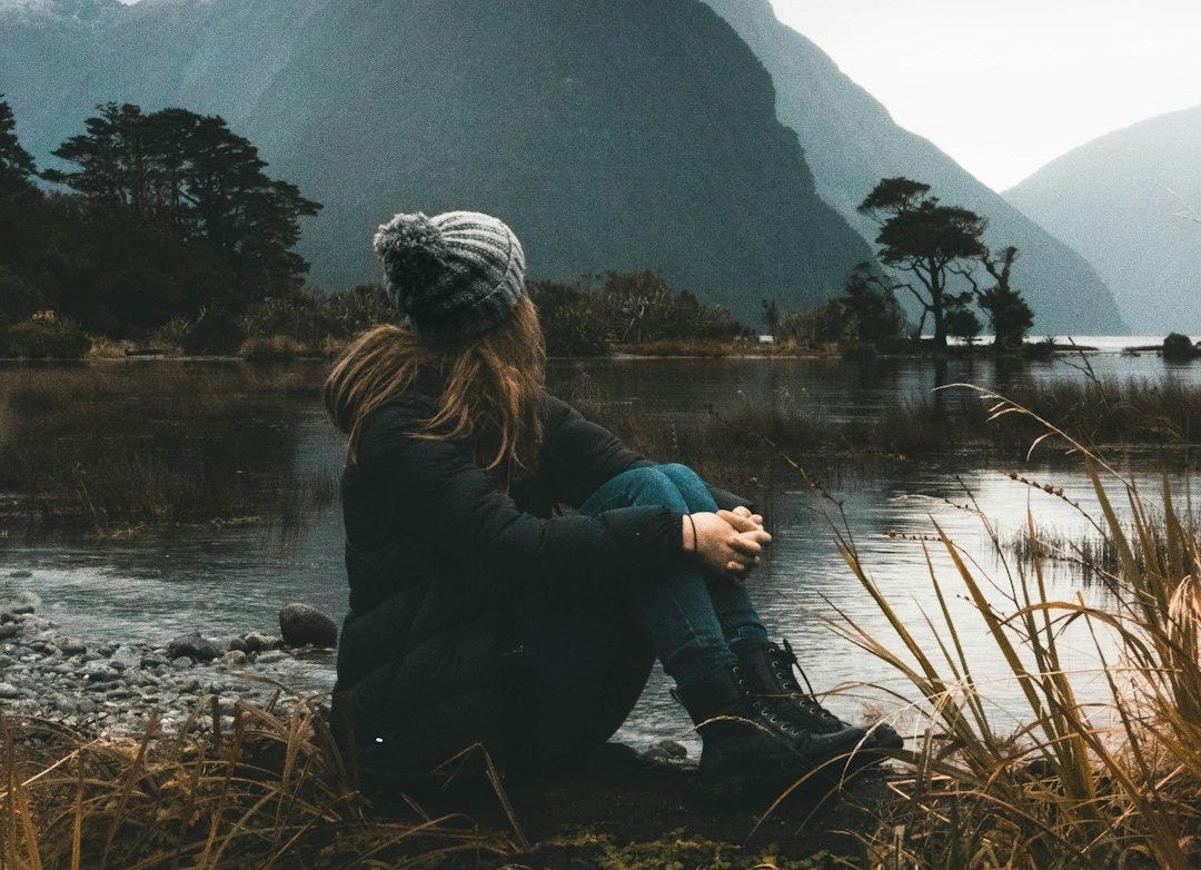 woman sitting near body of water looking at clouds woman sitting near body of water looking at clouds