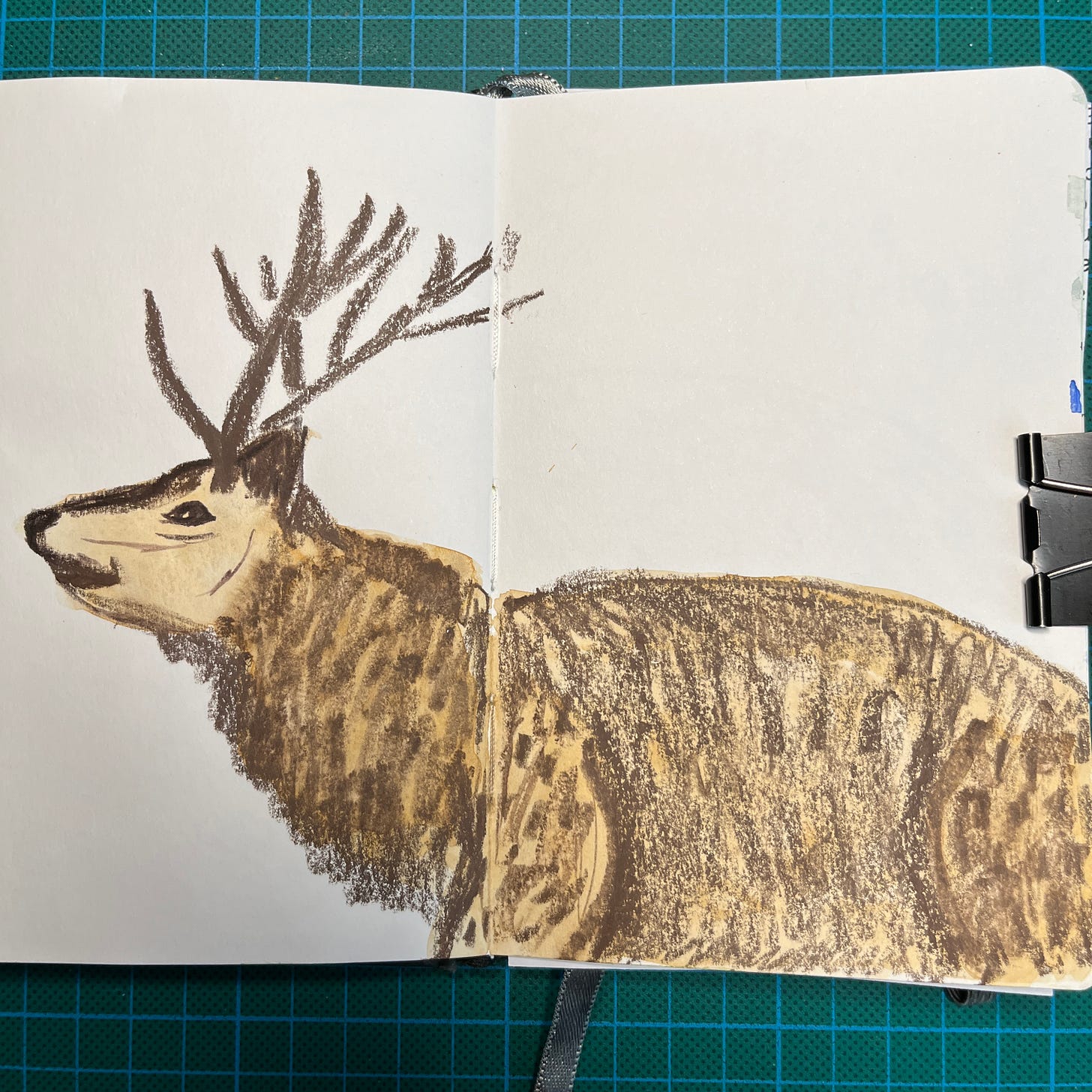 Posé sur mon tapis de découpe, mon sketchbook ouvert sur la double-page où j'ai fait le dessin du Jour 26 : un cerf. Posé sur mon tapis de découpe, mon sketchbook ouvert sur la double-page où j'ai fait le dessin du Jour 26 : un cerf.