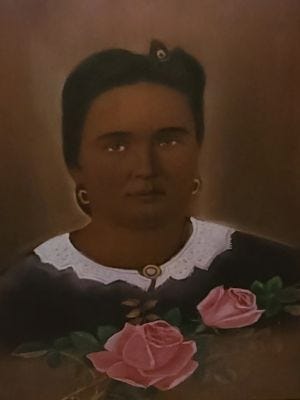 Painting of a woman with black hair, dark skin, light brown eyes. She has round gold earrings. Her dress is dark with a white collar. Two pink roses are painted at her chest. This is likely a memorial portrait done after her death in 1867. Painting of a woman with black hair, dark skin, light brown eyes. She has round gold earrings. Her dress is dark with a white collar. Two pink roses are painted at her chest. This is likely a memorial portrait done after her death in 1867.
