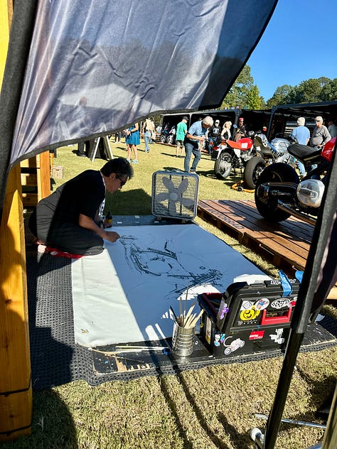 an artist doing a large live sketch of a concept bike; the race track; vintage bikes, and a cigar